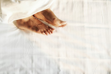 Feet in comfortable bed. Close up of feet in a bed under white blanket. Bare feet of a woman peeking out from under the cover.Top view with copy space (selective focus).