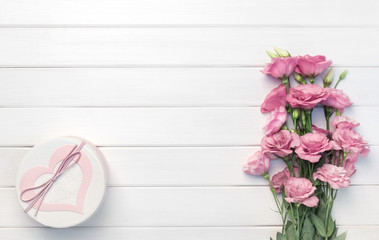 Beautiful pink eustoma flowers and handmade gift box on white wooden background. Copy space, top view,