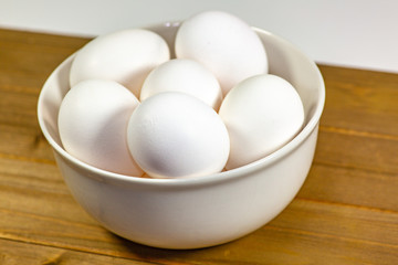 A group of eggs inside a deep white bowl next to a whisk waiting for the chef to use them in a meal