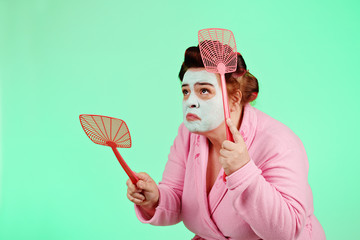 femme ronde et drôle avec bigoudis chassant les mouches avec tapette  