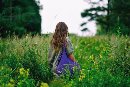 Woman With Long Haor Walking On Field With Bag Alone.