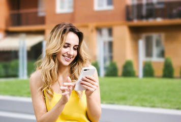 Fototapeta premium smiling girl with smartphone. Texting, chatting. Social media, communication people, photo, gadget addicted concept. Multistory house, building block on background