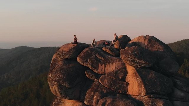 Epic drone shot of friends enjoy the sunset sitting on top of a high mountain in the Siberian Stolby nature reserve.