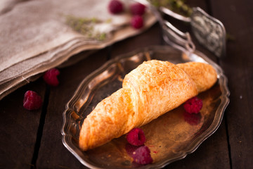 Golden fresh croissant on old wooden background close up with raspberry
