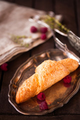 Golden fresh croissant on old wooden background close up with raspberry