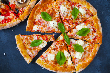 Homemade pizza with tomatoes, mozzarella and basil. Top view with copy space on dark stone table.