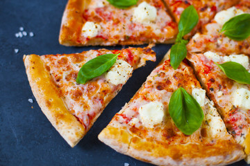 Homemade pizza with tomatoes, mozzarella and basil. Top view with copy space on dark stone table.