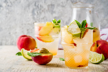Peach and lime lemonade, mojito cocktail with fresh fruit garnish, om light concrete background copy space selective focus