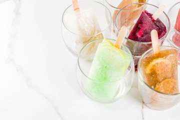 Summer party food ideas, frozen boozy alcohol cocktails popsicles - Prosecco, Vodka lime mojito, Champagne, Bellini, Margarita, Negroni etc white marble table copy space