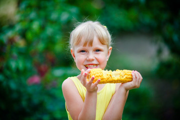 The cheerful girl eats corn on a farm.