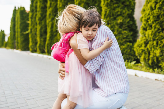Horizontal image of beautiful mother with love hugging her cute daughter in the street next to the home. Good relationship support. Sad little girl embracing her mom before the preschool day