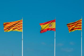 Catalonian, Spanish and Tarragonian flags flying on a mast against a blue sky