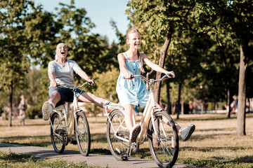 Fototapeta premium Joyful mood. Happy female person expressing her emotions and holding hands on the handle bar while walking in park