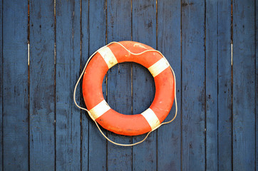 Old orange and white lifebuoy on a dark wooden background. Planked wooden dark blue wall texture