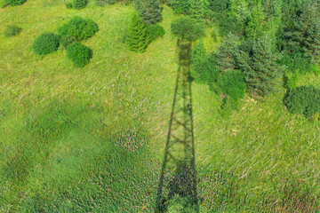 Shadow of telecommunication tower with radio antennas and satellite dishes on the green field with...