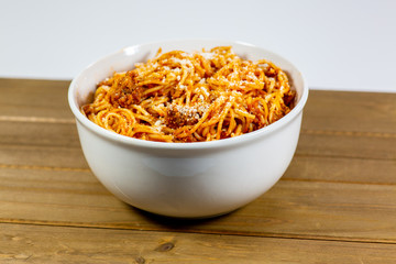 Spaghetti Bolognese in a deep white bowl on the wooden kitchen table waiting to be eaten