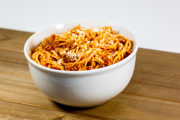 Spaghetti Bolognese in a deep white bowl on the wooden kitchen table waiting to be eaten