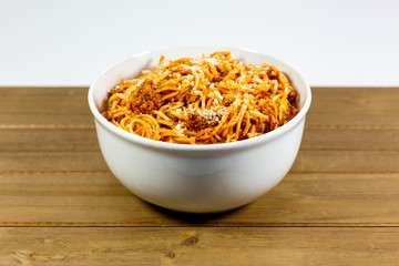 Spaghetti Bolognese in a deep white bowl on the wooden kitchen table waiting to be eaten