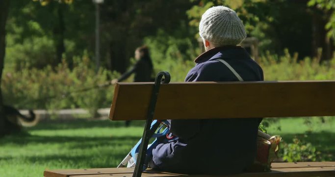An old lady is sitting on the bench in a city park