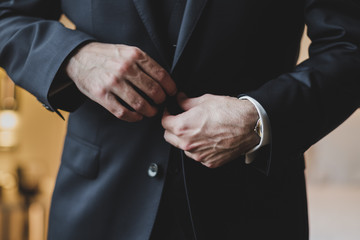 Detail of groom getting ready for wedding ceremony, closing jacket button
