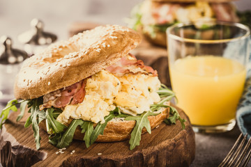 Sesame seeds Whole Grain bagels with scrambled eggs, rucola and fried bacon on small wooden...