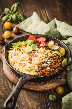 Delicious spaghetti Bolognaise or Bolognese with savory minced beef and cherry tomatoes garnished with parmesan cheese and basil in cost iron pan. Healthy italian food. Retro style toned.