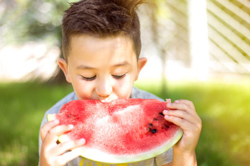 Happy child eating watermelon in the garden. Boy with fruit outdoors park.