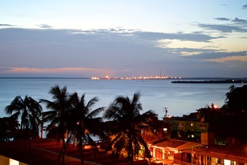 The sun sets in the Caribbean sea with palm trees at the foreground, in Cienfuegos Cuba
