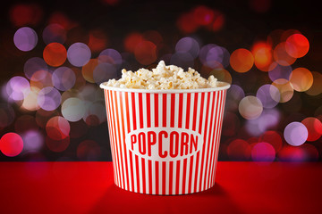 Bucket with tasty popcorn and blurred lights on background. Cinema evening