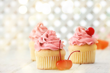 Delicious vanilla cupcakes and cherries on table