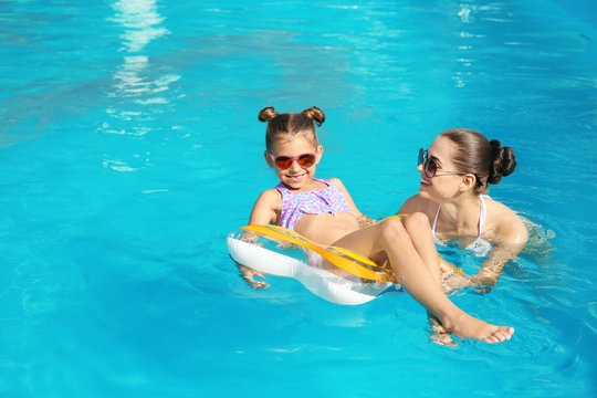 Young mother with little daughter in swimming pool on sunny day
