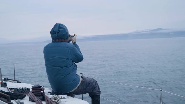 Man making photo of landscape during sea voyage on sailing ship back view