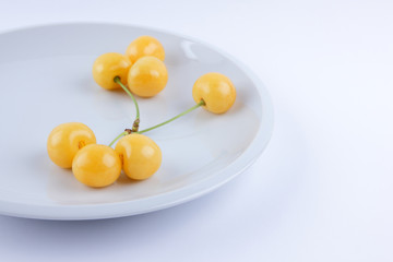 Yellow cherries on white plate, fresh cherries on white background, yellow berries in minimalism style, vegetarian food, isolated