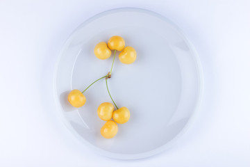 Yellow cherries on white plate, fresh cherries on white background, yellow berries in minimalism style, vegetarian food, isolated