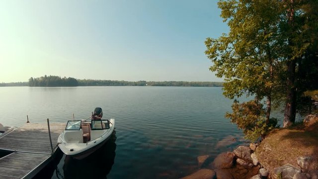 Beautiful slow wide angle panning shot of a lake with a dock and boat in the foreground in the morning sun