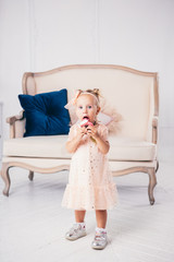 Obraz premium children's birthday. funny two-year-old Caucasian girl in pink dress standing to bedroom of house the background of couch and eating, holding cake dessert. Face and mouth smeared, smeared with cream