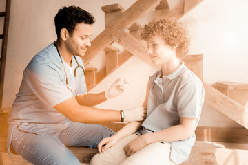 Keep calm. Delighted medical worker holding syringe and sitting in semi position while looking at relaxed arm