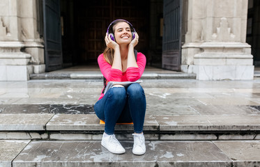 Young student woman listening to music with a headphones sitting on the stairs