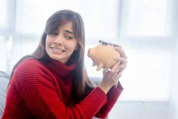 Sad woman showing an empty piggy bank at home