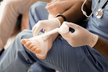 Dressing leg. Competent doctor sitting in semi position and being well equipped while changing bandage