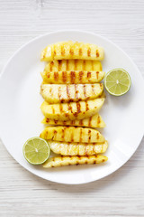Grilled pineapple slices with lime on white plate over white wooden surface, top view. Summer food. Idea for snack. From above, overhead.