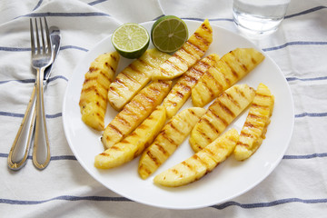 Grilled pineapple wedges with lime on white plate, side view. Summer food.