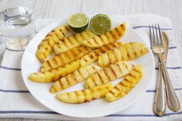 Grilled pineapple wedges with lime and glass of water, side view. Summer food.