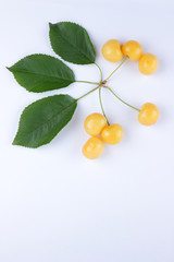 Yellow cherries on a white background, fresh cherries with green leaves, yellow berries in minimalism style, vegetarian food, blank for designer