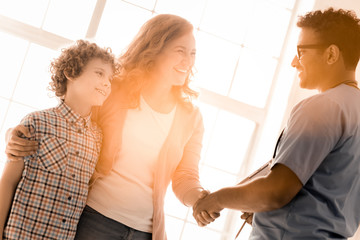 Obraz premium Nice to meet you. Happy female expressing positivity and embracing her son while shaking hands with medical worker