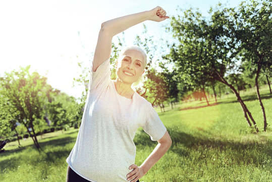 Useful exercise. Cheerful smiling energetic pensioners looking happy while doing exercises in a green park