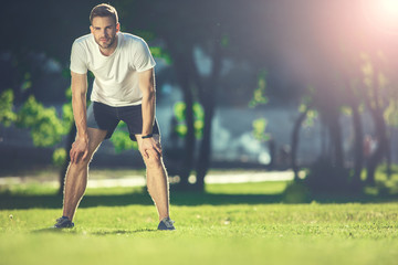 Full length portrait of focused sportsman training in park. He is bending forward and putting hands...