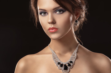 Portrait of beautiful young woman with luxury jewelry on dark background