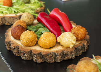 fried balls with cheese in breadcrumbs with greens and fresh paprika on a tree on a dark table