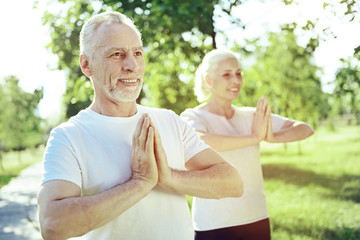 Practicing together. Cheerful smiling aged couple being happy while practicing yoga together